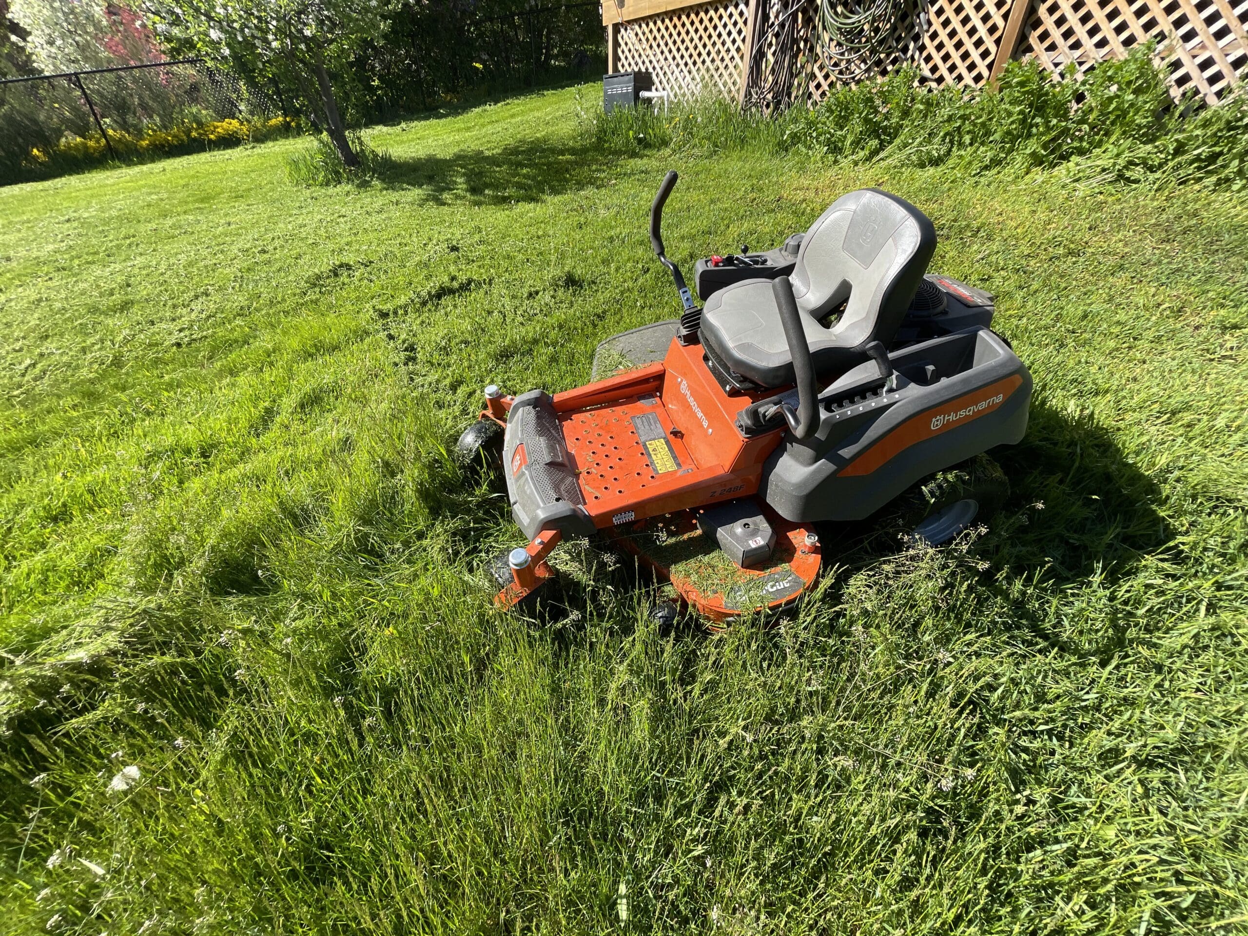 mower in long grass part way through mowing a lush green yard